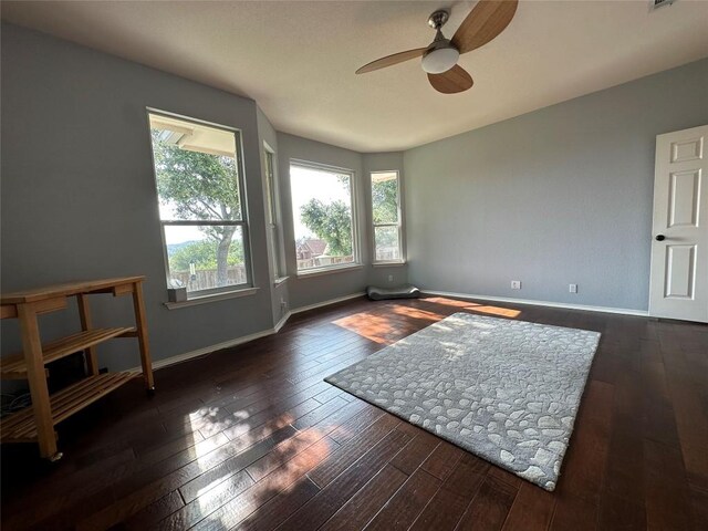 empty room with baseboards, a ceiling fan, and dark wood-style floors