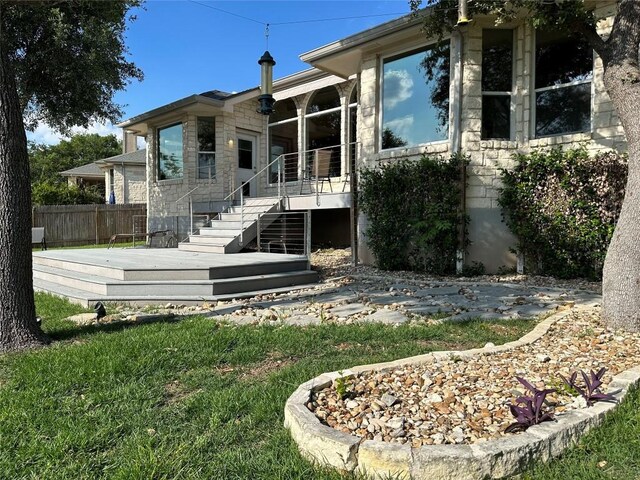 back of property with fence, a lawn, a wooden deck, and stone siding