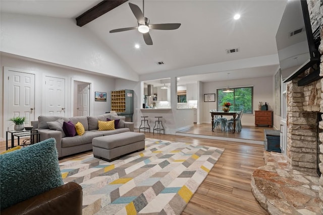 living room featuring light wood finished floors, visible vents, beamed ceiling, high vaulted ceiling, and ceiling fan