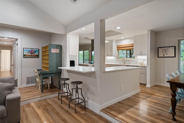kitchen featuring a breakfast bar, light wood-style floors, backsplash, and white cabinets