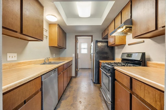 kitchen with a sink, concrete flooring, a raised ceiling, wall chimney exhaust hood, and appliances with stainless steel finishes