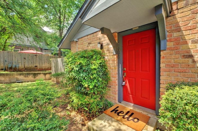 view of exterior entry featuring fence and brick siding