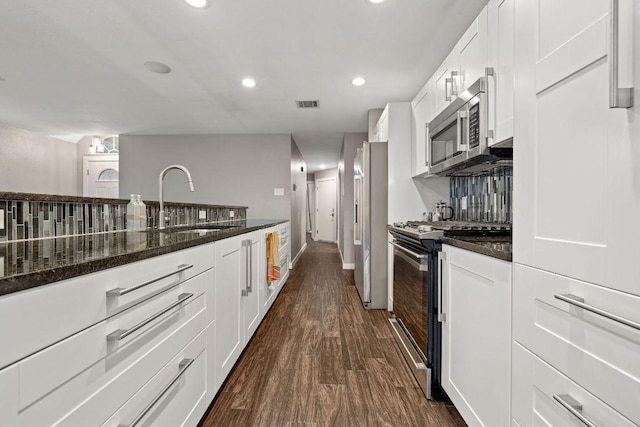 kitchen with dark stone countertops, a sink, stainless steel appliances, white cabinetry, and visible vents