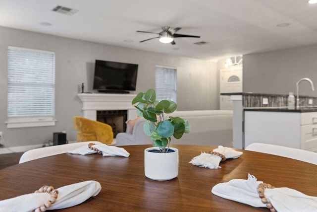 dining space with a ceiling fan, wood finished floors, visible vents, and a fireplace