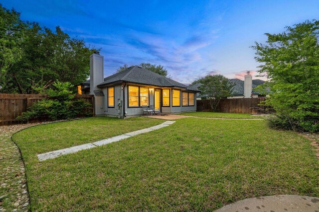 rear view of property with a fenced backyard, a chimney, and a yard