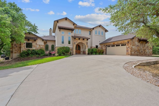 mediterranean / spanish house featuring stucco siding, an attached garage, stone siding, and curved driveway