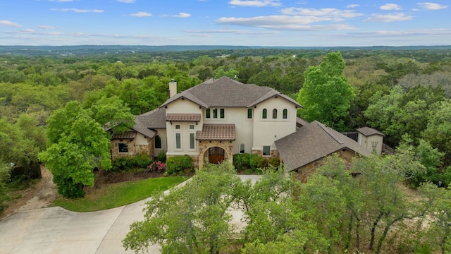 view of front of home with a chimney, a view of trees, stone siding, and stucco siding