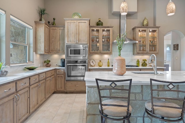kitchen with light stone countertops, a sink, stainless steel appliances, decorative backsplash, and arched walkways