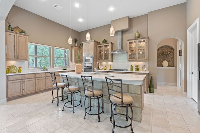 kitchen with a kitchen breakfast bar, light countertops, wall chimney range hood, a sink, and appliances with stainless steel finishes