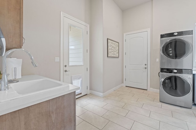 clothes washing area with light tile patterned floors, stacked washer and dryer, baseboards, and a sink