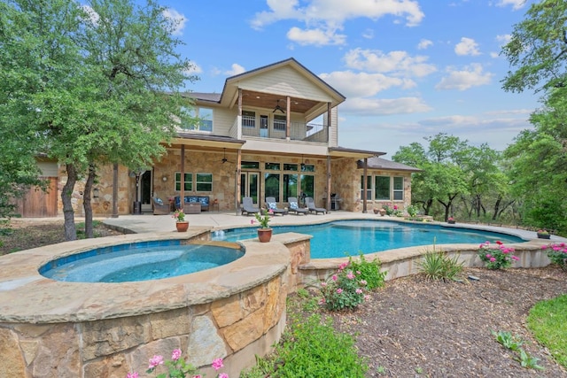 rear view of house with stone siding, a ceiling fan, a balcony, and an in ground hot tub