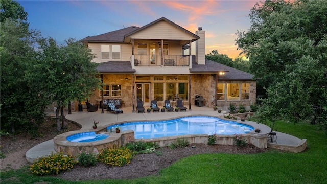 16016 Palomino Ranch Dr, Leander, TX 78641 - back of house at dusk with a balcony, ceiling fan, stone siding, a chimney, and a patio area