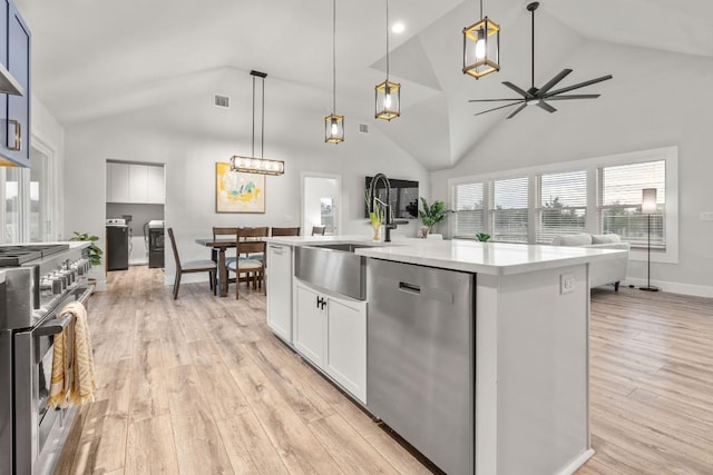 kitchen with a sink, open floor plan, ceiling fan, stainless steel appliances, and light wood finished floors