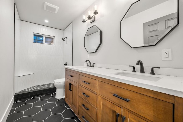 bathroom with a tile shower, tile patterned floors, double vanity, toilet, and a sink