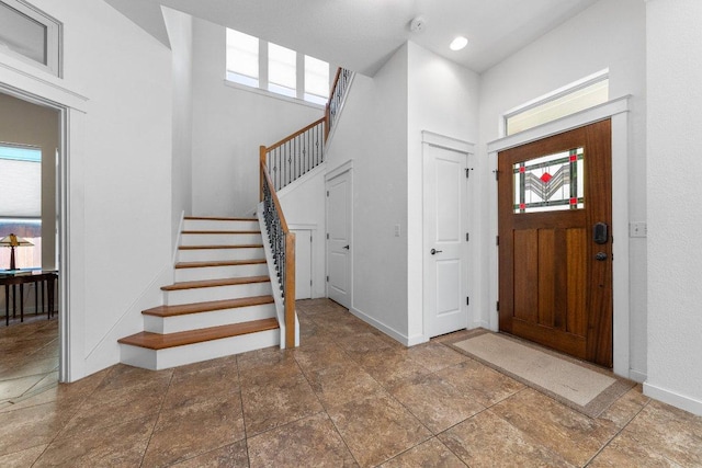 foyer entrance with baseboards, a high ceiling, stone finish floor, and stairs
