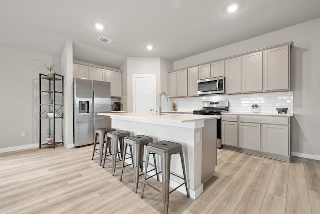 kitchen featuring light wood-style floors, a kitchen bar, gray cabinets, and stainless steel appliances