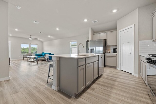 kitchen featuring decorative backsplash, stainless steel appliances, gray cabinetry, and a sink