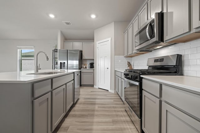 kitchen featuring stainless steel appliances, visible vents, gray cabinets, a sink, and light wood-type flooring