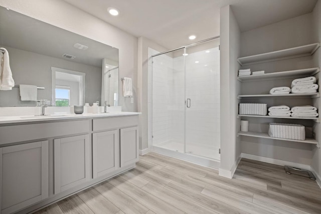 full bathroom featuring a shower stall, double vanity, wood finished floors, a sink, and baseboards