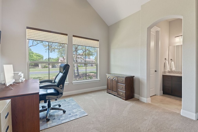 office area featuring arched walkways, a healthy amount of sunlight, and light carpet