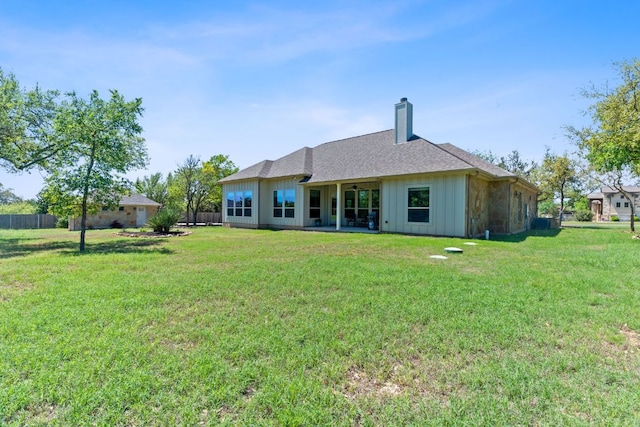 back of house featuring board and batten siding, a chimney, fence, and a yard