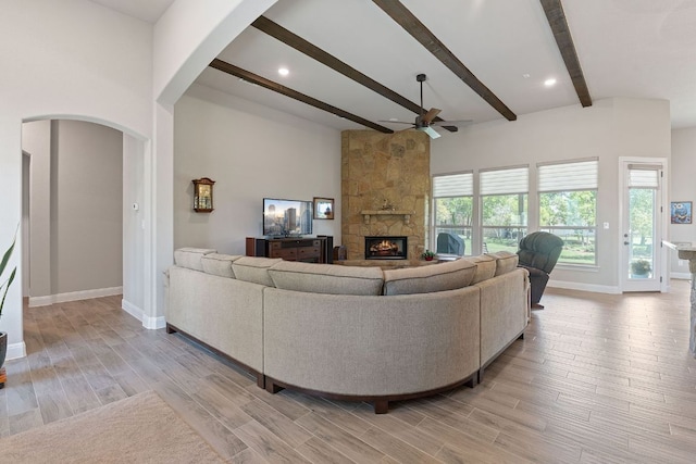 living area featuring beamed ceiling, a stone fireplace, baseboards, and ceiling fan