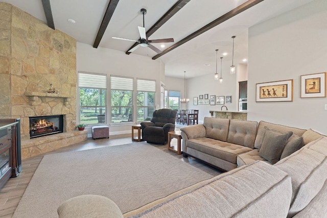 living area with a fireplace, a ceiling fan, lofted ceiling with beams, and light wood-type flooring