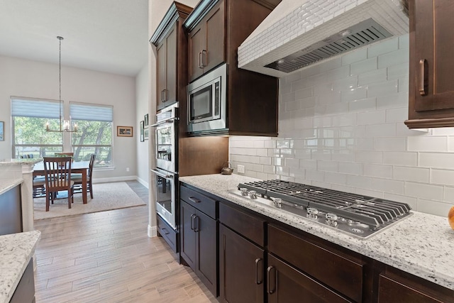 kitchen with wall chimney exhaust hood, stainless steel appliances, dark brown cabinets, baseboards, and decorative backsplash