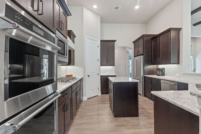 101 Dakota Dr, Georgetown, TX 78633 - kitchen featuring appliances with stainless steel finishes, light stone counters, dark brown cabinetry, arched walkways, and decorative backsplash