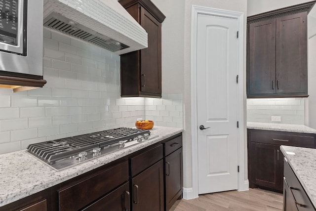 101 Dakota Dr, Georgetown, TX 78633 - kitchen featuring stainless steel gas stovetop, custom exhaust hood, dark brown cabinets, decorative backsplash, and light wood finished floors