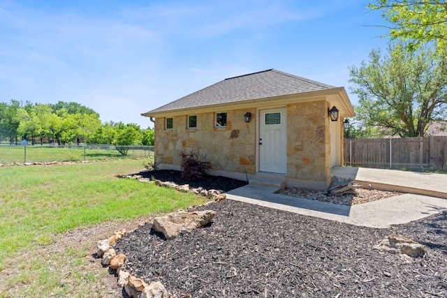 exterior space featuring a yard, stone siding, a fenced backyard, and a shingled roof