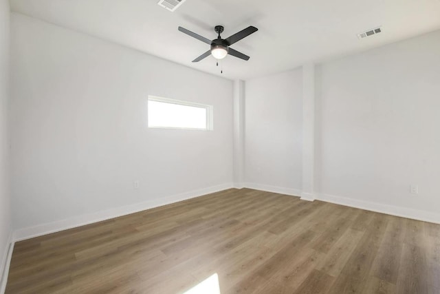 spare room featuring wood finished floors, visible vents, a ceiling fan, and baseboards