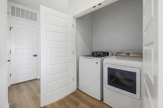 clothes washing area with washing machine and dryer, light wood-style flooring, visible vents, and laundry area
