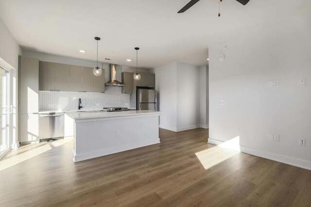 kitchen featuring backsplash, gray cabinetry, wall chimney range hood, light countertops, and appliances with stainless steel finishes