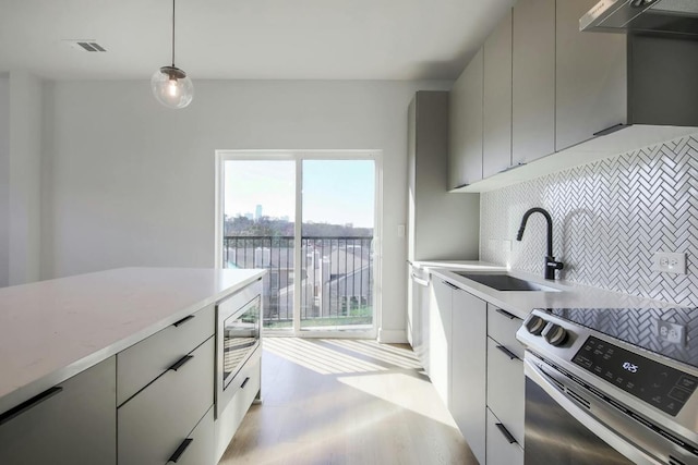 kitchen featuring stainless steel appliances, gray cabinets, modern cabinets, a sink, and tasteful backsplash