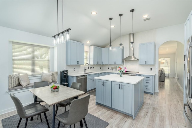 129 Aguilar Dr, Hutto, TX 78634 - kitchen with appliances with stainless steel finishes, wall chimney range hood, arched walkways, light countertops, and a kitchen island