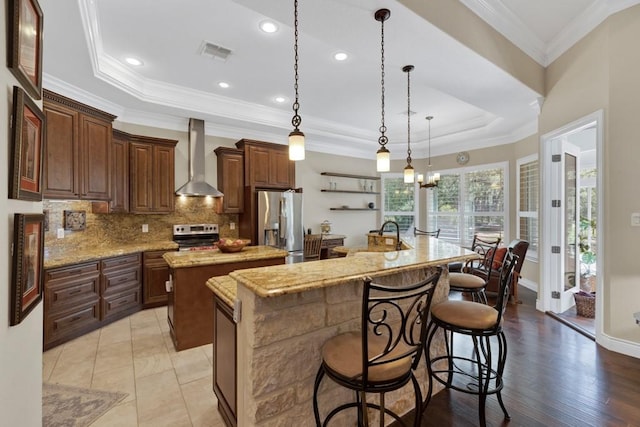 1164 Fairway Dr, Canyon Lake, TX 78133 - kitchen featuring stainless steel appliances, a tray ceiling, a center island with sink, wall chimney exhaust hood, and visible vents