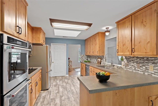 104 Tonkawa Cv, Kyle, TX 78640 - kitchen with stainless steel appliances, a sink, light wood-style floors, backsplash, and a skylight