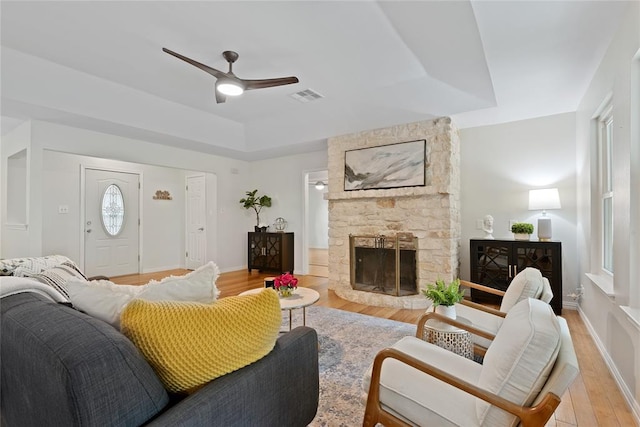 104 Tonkawa Cv, Kyle, TX 78640 - living area featuring a ceiling fan, a stone fireplace, light wood finished floors, a raised ceiling, and visible vents