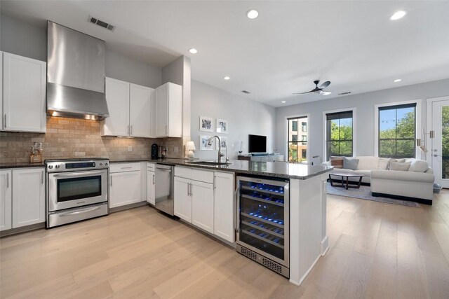 kitchen with a sink, open floor plan, beverage cooler, stainless steel appliances, and wall chimney exhaust hood