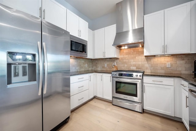 kitchen featuring white cabinets, stainless steel appliances, dark stone counters, and wall chimney range hood