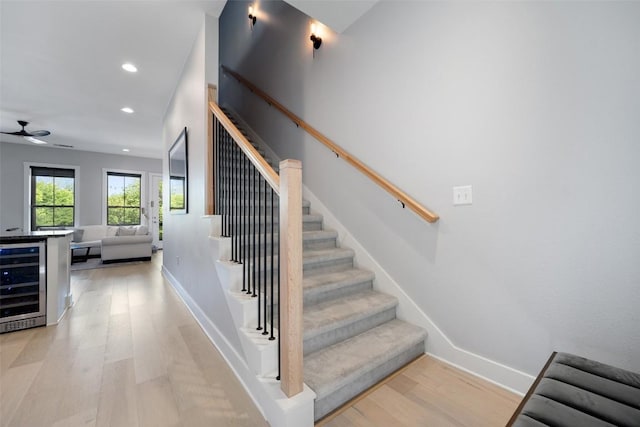 stairs with baseboards, a ceiling fan, wood finished floors, and wine cooler