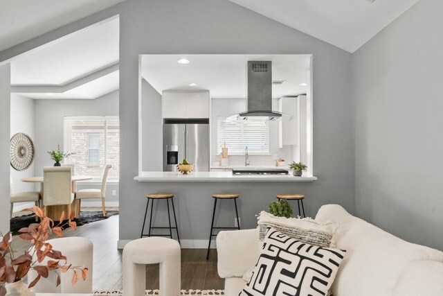 kitchen featuring stainless steel fridge, vaulted ceiling, island range hood, and wood finished floors