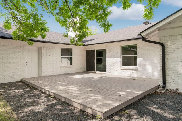 back of property with a shingled roof, brick siding, and a deck