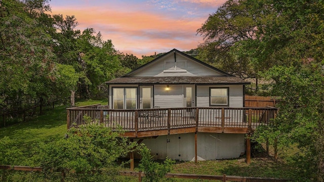 back of property at dusk with a wooden deck and fence