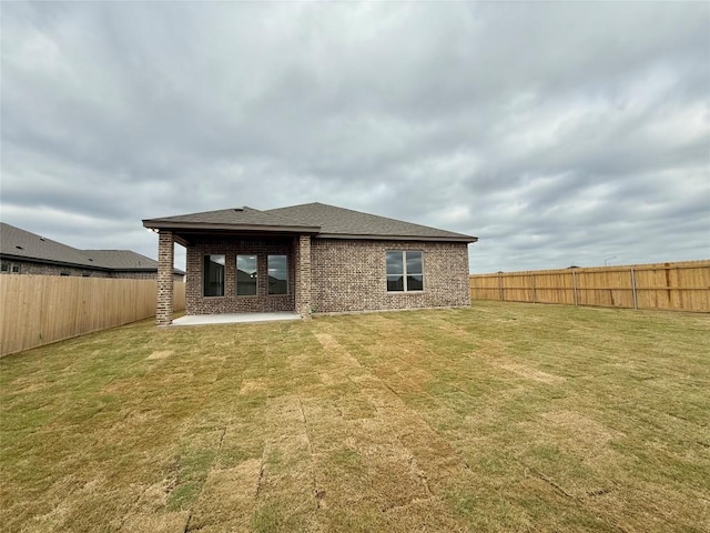 rear view of property featuring a fenced backyard, a yard, roof with shingles, a patio, and brick siding