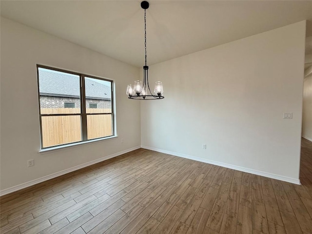 empty room with a notable chandelier, baseboards, and dark wood-style flooring