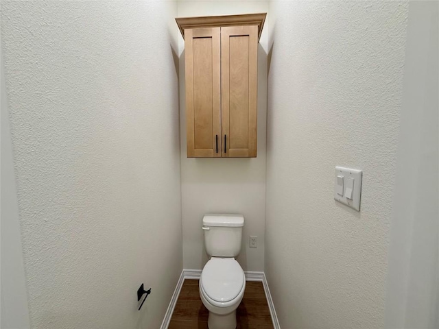 bathroom featuring baseboards, wood finished floors, and toilet