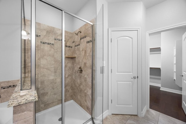 full bath with a walk in closet, a shower stall, tile patterned flooring, and baseboards
