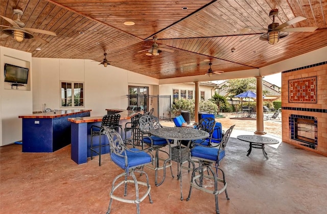 view of patio featuring a ceiling fan, exterior fireplace, fence, and exterior bar